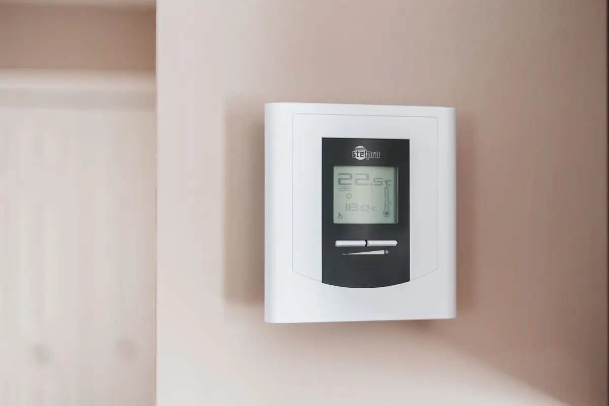 A white digital thermostat mounted on a pale interior wall.